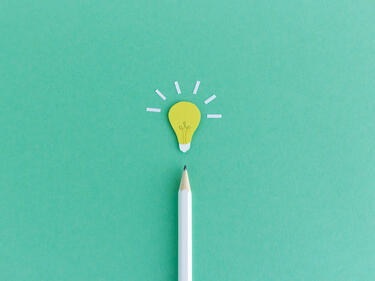 Creative composition of pencil with small paper light bulb glowing above on green background